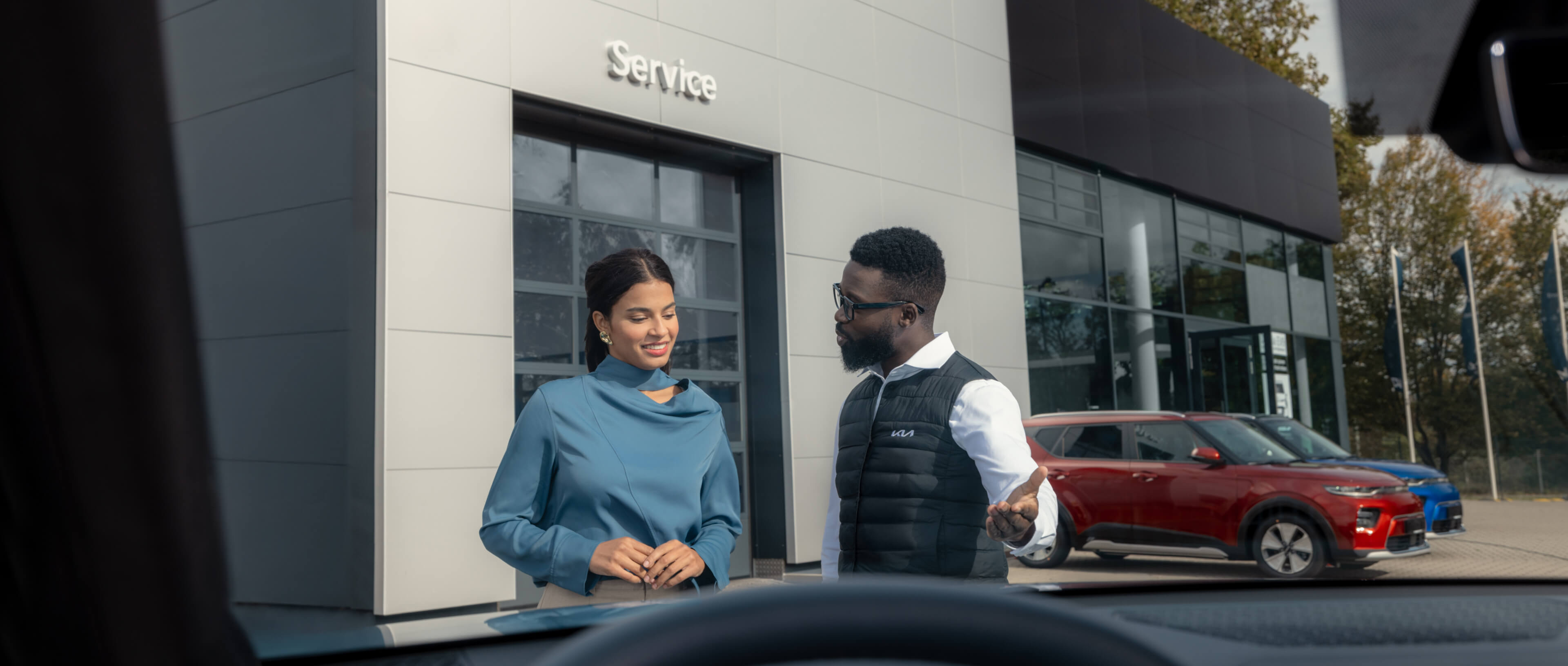 Serviceversprechen, Service-Mitarbeiter und Kundin stehen vor einer Kia Service-Werkstatt